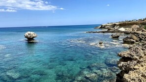 A coastal scene with clear blue water, rocky formations, and a distant shoreline. - Anchora___ (Paralimni)