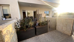 A modern building with a stone facade, a gated entrance, and a small garden area with plants and a seating area. - Anchora___ (Paralimni)
