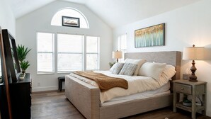 Quarto com cama, duas mesas de cabeceira, abajur, moldura de quadro e janela com persianas.