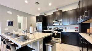 A modern kitchen with dark cabinets, stainless steel appliances, and a central island with bar stools. - NEW! 2 Pools + Gym, Kids Water Playground, Near Disney {Chic Retreat} (Davenport)