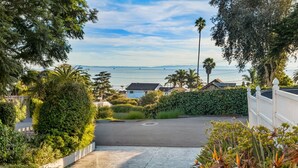 A residential area with a paved driveway leading to a house, surrounded by lush greenery and a view of the ocean. - 5BR Beach House | Hot Tub, Game Room + Studio (Summerland)