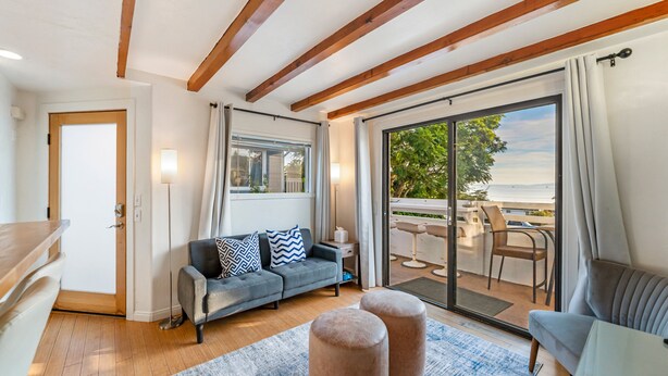 A modern living room with a sofa, ottomans, a dining area with chairs, and a view of the outdoors. - 5BR Beach House | Hot Tub, Game Room + Studio (Summerland)