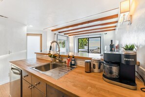 A modern kitchen with a wooden countertop, stainless steel sink, and a Keurig coffee maker. - 5BR Beach House | Hot Tub, Game Room + Studio (Summerland)