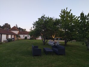 Eine begrünte Außenanlage mit Sitzgelegenheiten, einem Gebäude mit rotem Dach und Bäumen.