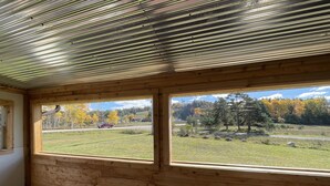Ein Zimmer mit Holzwänden und einem großen Fenster mit Blick auf eine Straße und Herbstbäume.