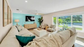 A modern living room with a teal accent wall, a large window with a view, and a cozy seating area. - Pool, hot tub, putting green, pickleball, tiki bar, fire pit (Bradenton)