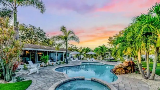 A swimming pool with a hot tub, surrounded by palm trees and a patio area with lounge chairs. - Pool, hot tub, putting green, pickleball, tiki bar, fire pit (Bradenton)