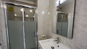 Ein Badezimmer mit einer Duschkabine aus Glas, einem weißen Waschbecken und einem Spiegel.
