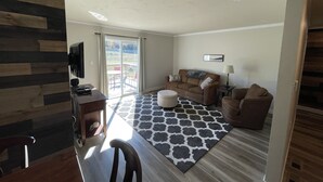 A living room with a sofa, a coffee table, and a TV. There is a sliding glass door leading to an outdoor area with chairs. - Scenic 2BR by Pine Mountain - Ski Hill + Golf Course (Iron Mountain)