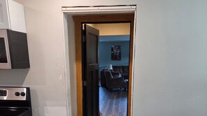 A kitchen with a microwave and stove, a wooden floor, and a doorway leading to a living room with a couch and a lamp. - Scenic 2BR by Pine Mountain - Ski Hill + Golf Course (Iron Mountain)