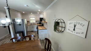 A modern kitchen with white cabinets, a wooden dining table, and a wall-mounted sign advertising ski lodge rentals and lessons. - Scenic 2BR by Pine Mountain - Ski Hill + Golf Course (Iron Mountain)