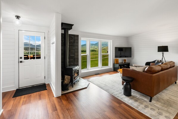 A living room with a fireplace, a sofa, a TV, and a view of the outdoors. - Paradise Valley-Mountain Escape (Emigrant)