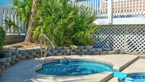 Una piscina con borde de piedra, una escalera metálica y una valla blanca al fondo.