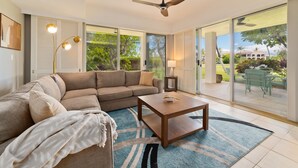 A modern living room with a sectional sofa, a wooden coffee table, and a large sliding glass door leading to an outdoor patio. - Waikoloa Saltwater Haven in Vistas (Waikoloa)