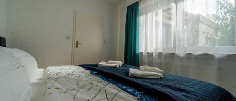 A hotel room with a bed, a window with curtains, and a door.