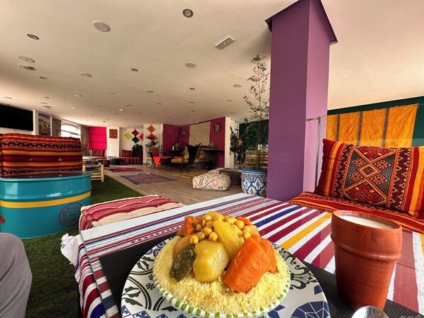 A room with a dining table set with a meal, a colorful striped sofa, and a large window with curtains. - Au Coeur de la Ville de Tanger (Tanger)