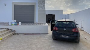 Ein modernes Gebäude mit geschlossener Garagentür, einem geparkten Auto und Baumaterialien am Boden.