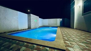 Ein Schwimmbecken mit Fliesenbord, einer Steinmauer und Nachthimmel.