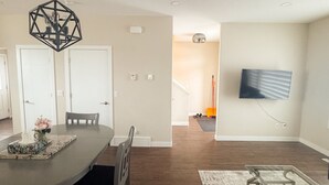 Een moderne woonkamer met een eetgedeelte, een wandtelevisie en een trap naar een andere verdieping.