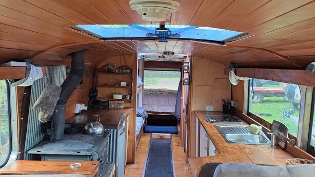 Interior compacto de una caravana con kitchenette, una pequeña zona de estar y una litera.