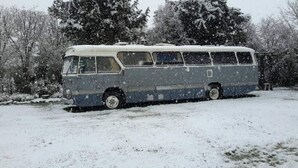 Un autobús antiguo estacionado en una zona nevada, con árboles al fondo.