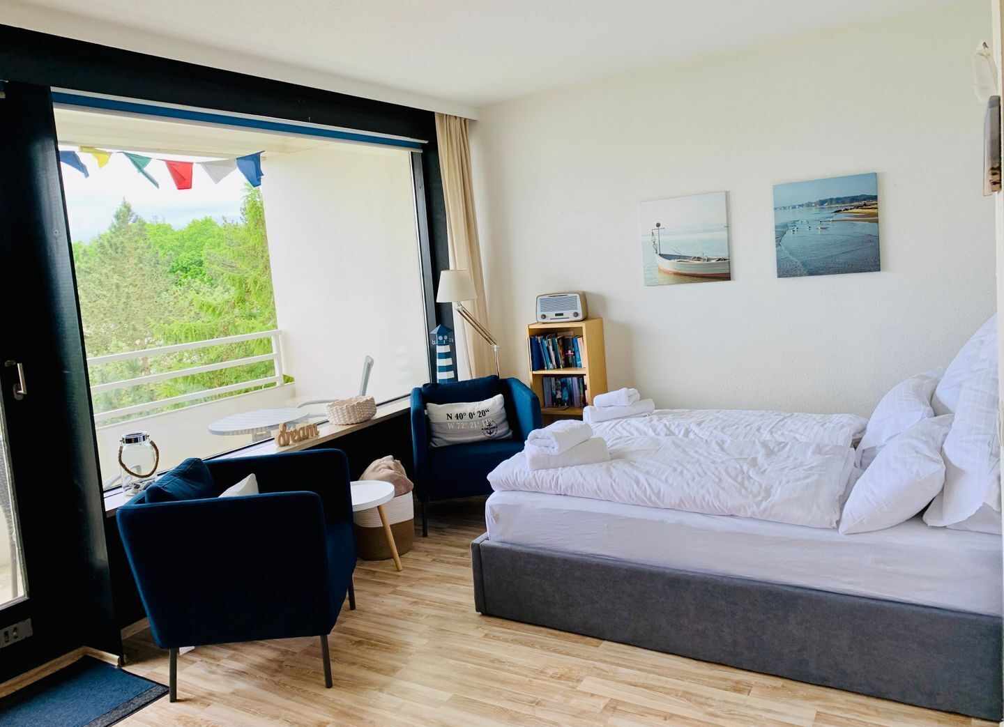 A room with a bed, a desk, a chair, a bookshelf, and a window with a view of greenery.