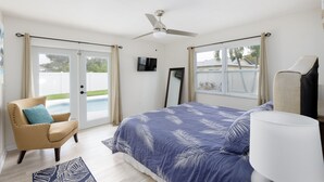 Een slaapkamer met een bed, een stoel, een plafondventilator, een televisie en uitzicht op een zwembad.