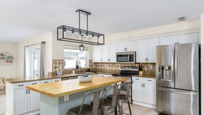Een moderne keuken met witte kasten, een houten eiland, roestvrijstalen apparatuur en een hanglamp.