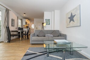 A modern living room with a grey sofa, a glass coffee table, and a dining area with a table and chairs.