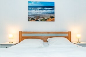 Un lit avec une tête de lit en bois, deux lampes de chevet et un tableau encadré représentant une scène de plage accroché au mur.