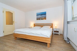 Une chambre à coucher avec un lit en bois, deux tables de chevet avec des lampes, une porte et un tableau au mur.