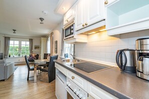 A modern kitchen with white cabinetry, a built-in microwave, a stove, and a coffee maker.