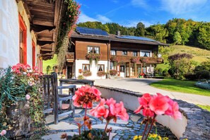 A traditional wooden building with a balcony, solar panels, and hanging flower baskets.