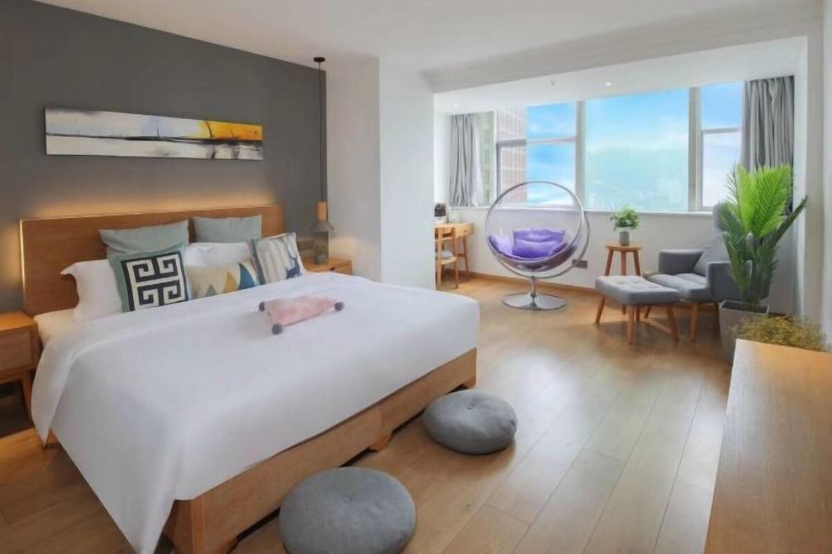 Et moderne hotelværelse med en stor seng, en hængestol, et skrivebord og udsigt til himlen.