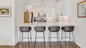 A modern kitchen with white cabinets, a stainless steel refrigerator, a built-in oven, and a large island with bar stools.