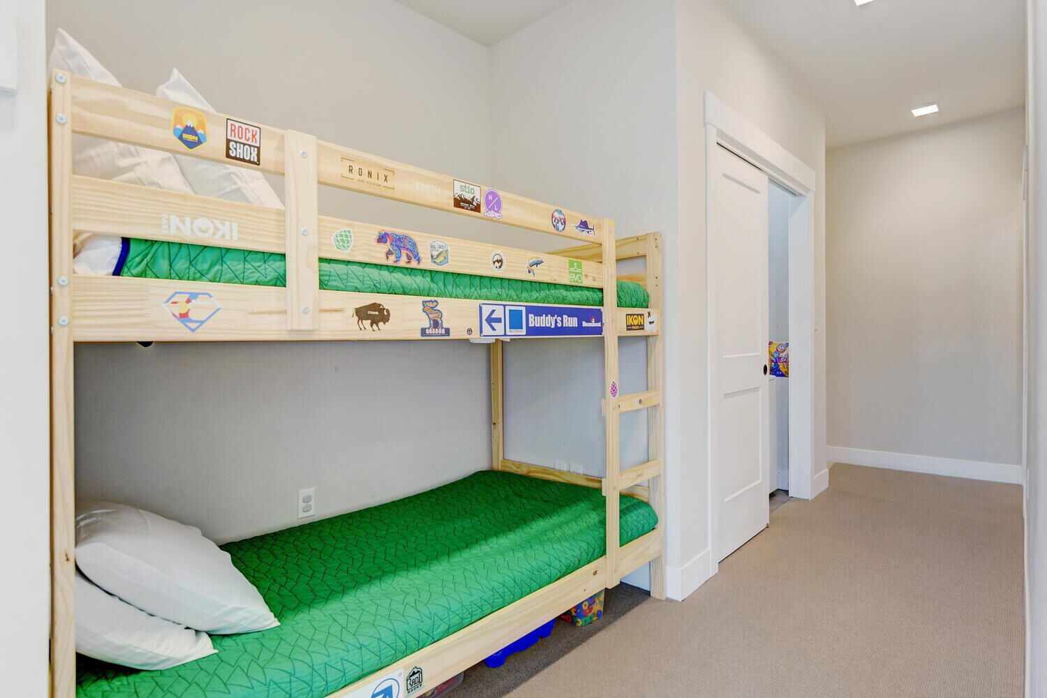 Habitación con literas, un colchón verde, una puerta blanca y un pasillo.