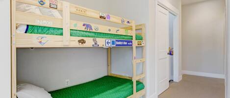 Habitación con literas, un colchón verde, una puerta blanca y un pasillo.