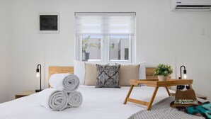 A hotel room with a bed, a bedside table with towels, a small table with a plant, and a window with blinds. - 2BR Countryside Home w/ Sea Views & Private Pool (Noord)
