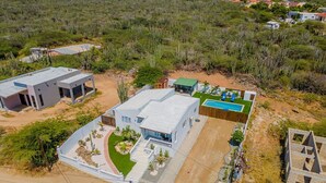 A large, modern house with a swimming pool, surrounded by a landscaped garden and a desert landscape. - 2BR Countryside Home w/ Sea Views & Private Pool (Noord)