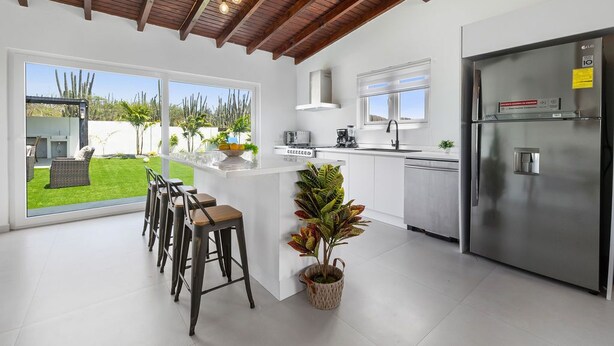A modern kitchen with a large island, stainless steel appliances, and a view of a lush garden. - 2BR Countryside Home w/ Sea Views & Private Pool (Noord)