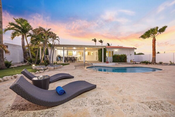 A poolside area with lounge chairs, a pool, and a building with a covered patio. - 4BR4BA w/ Private Pool ~ Walking distance to Ritz (Noord)