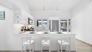A modern kitchen with white cabinetry, a stainless steel refrigerator, and a central island with bar stools. - 4BR4BA w/ Private Pool ~ Walking distance to Ritz (Noord)