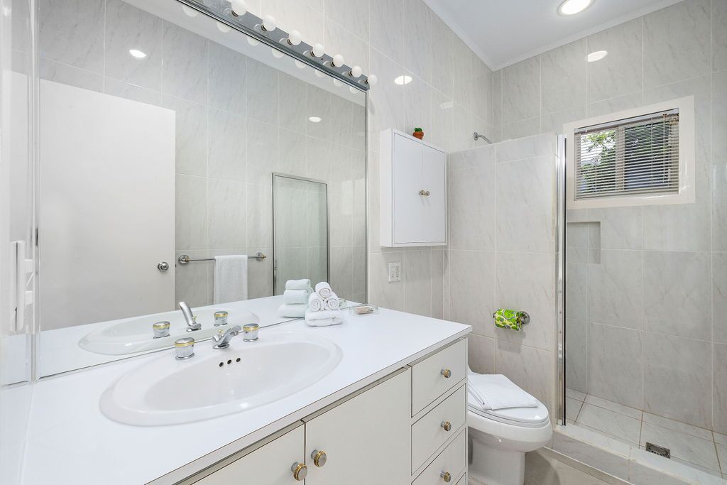 A modern bathroom with a large mirror, two sinks, a toilet, and a shower area.