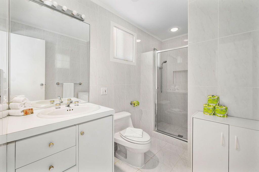 Un baño moderno con un espejo grande, lavabo blanco, inodoro y ducha.