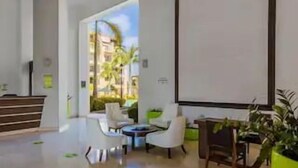 A spacious lobby with a reception desk, seating area, and a large window offering a view of palm trees. - Ground Floor 1BR Condo w/ Pool & Resort Amenities (Noord)