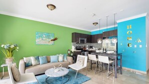 A modern living room with a green wall, a sofa, a coffee table, and a dining area with chairs and a table. - Ground Floor 1BR Condo w/ Pool & Resort Amenities (Noord)