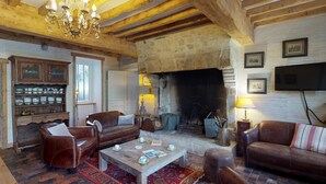 Un salon chaleureux avec des poutres apparentes, une cheminée, des canapés en cuir, une table basse et un buffet.