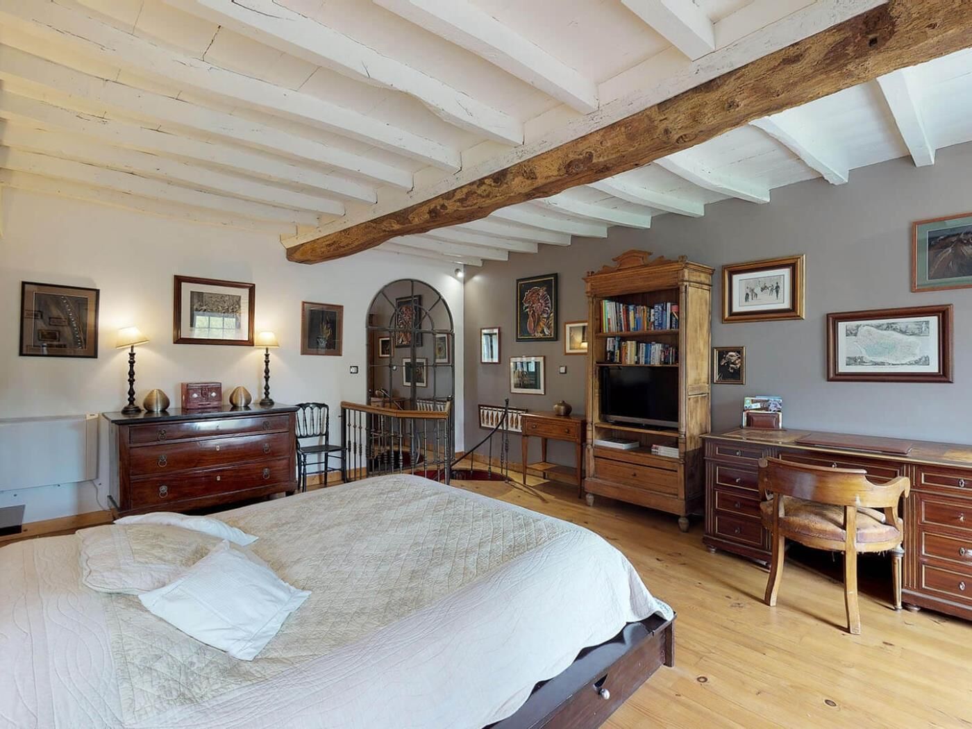 A bedroom with a large bed, wooden furniture, a TV, and various framed pictures on the walls.