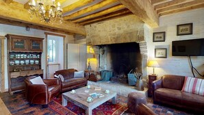 Uma sala de estar acolhedora com vigas de madeira, lareira, sofás de couro e uma mesa de centro.