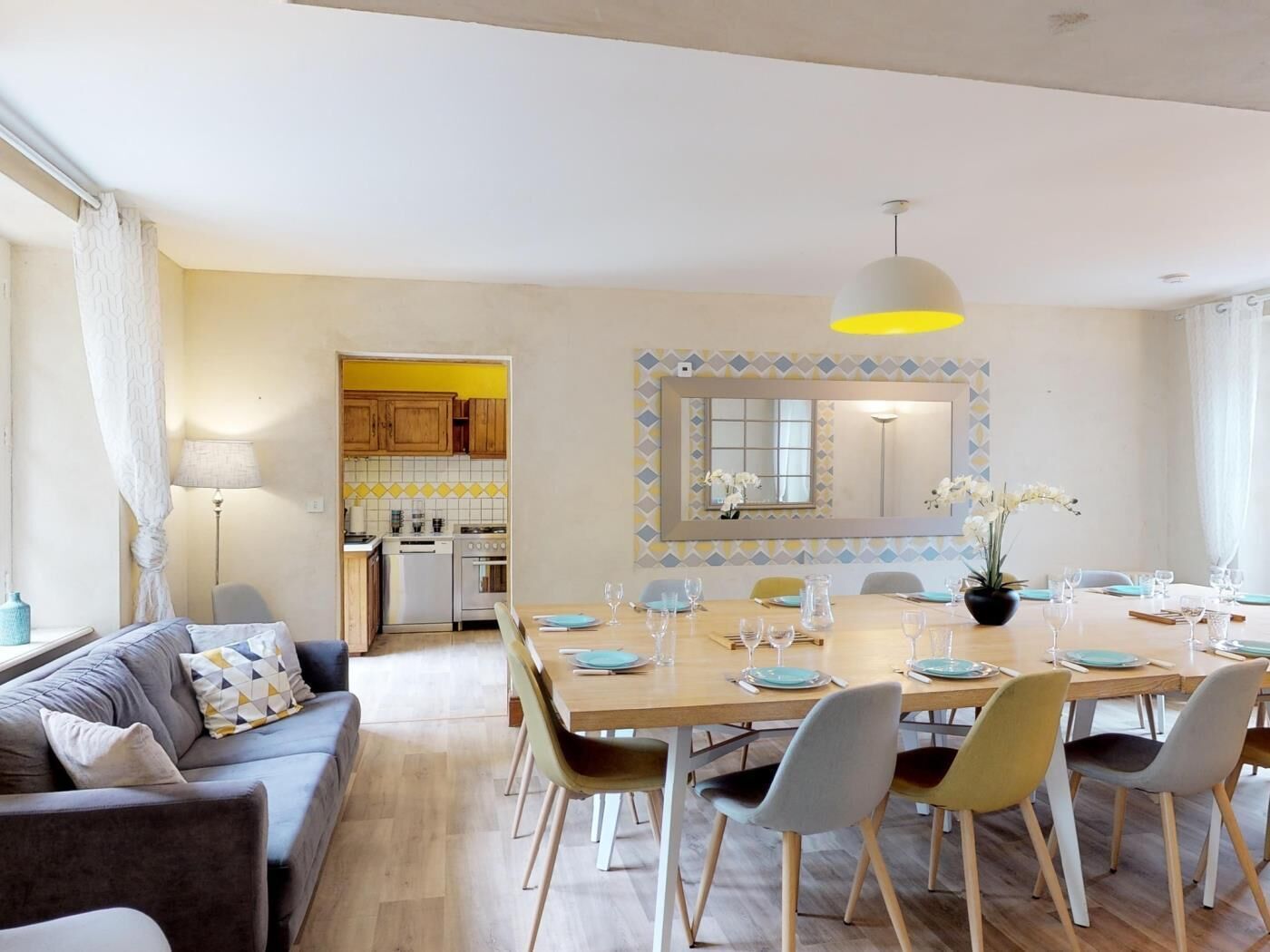 A modern living room with a sofa, dining table set for six, and a kitchen in the background.